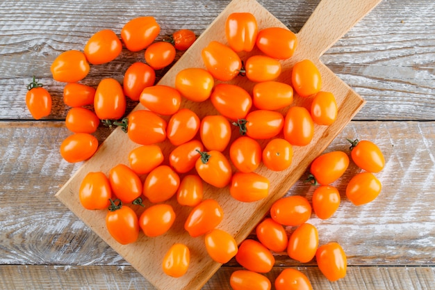 Mini tomates en tabla de cortar y madera. aplanada