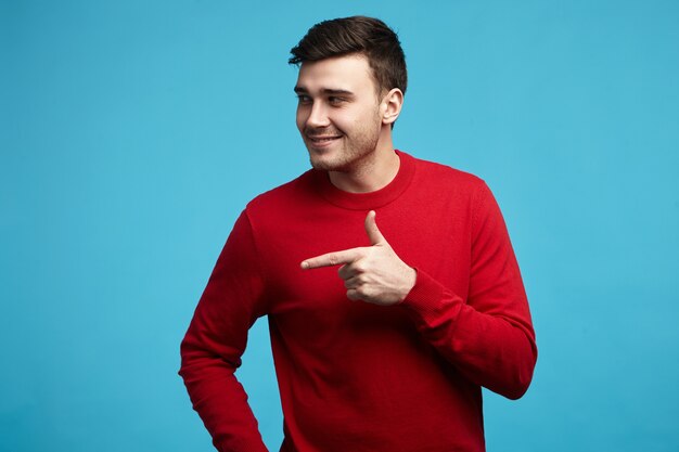 ¡Mira allá! Feliz atractivo joven con rastrojo posando contra la pared azul en blanco del estudio