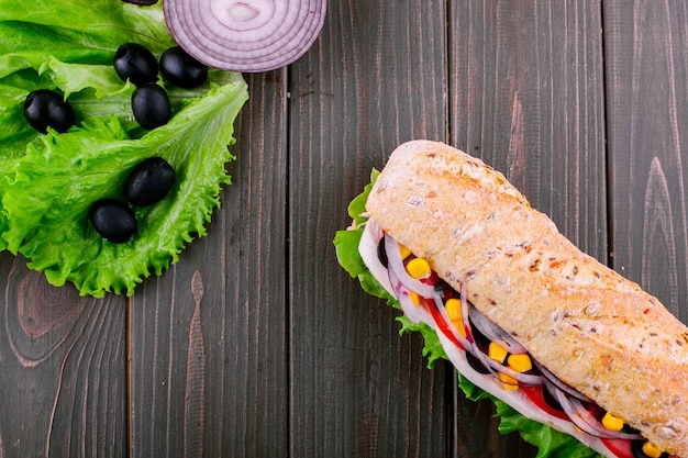 Mira desde arriba en la ensalada verde, piezas de cebolla azul y sándwich integral en la mesa de madera oscura