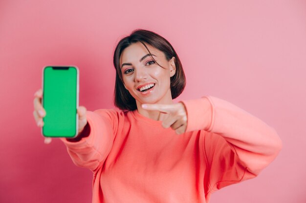 ¡Mira este celular! La mujer feliz y complacida señala con el dedo índice en la pantalla en blanco, muestra un dispositivo moderno, emociones felices y sorprendidas.