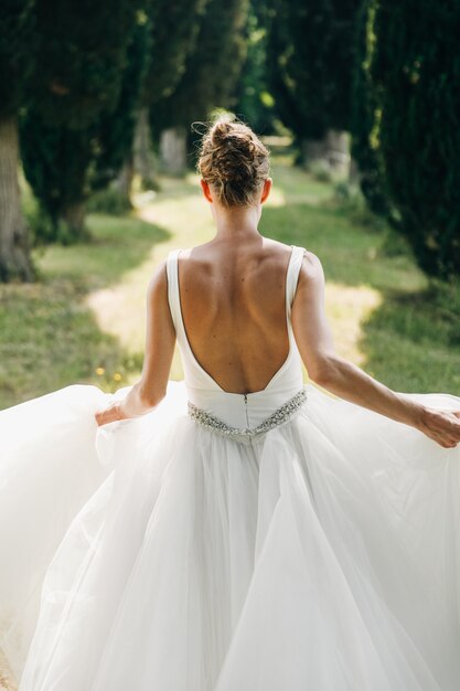 Mira por detrás a la novia vestida con la espalda desnuda corriendo a lo largo