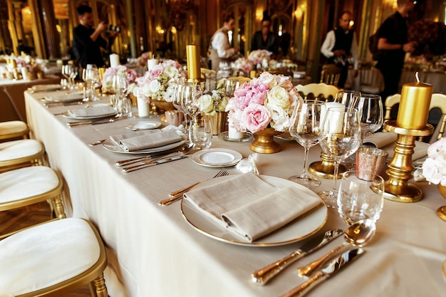 Mira desde lejos a la mesa servida con ricos cubiertos y vajilla, jarrones de oro y candelabros