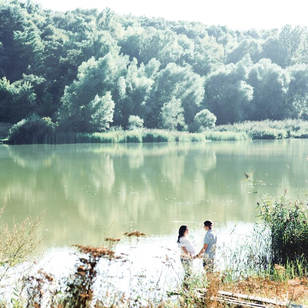 Mira desde lejos a una pareja encantadora, tomados de las manos mientras están de pie junto al río