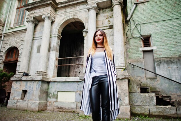 Mirada de mujer de moda con pantalones de cuero de chaqueta de traje de rayas blancas y negras posando en la calle vieja Concepto de chica de moda