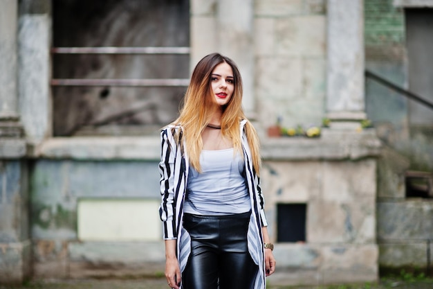 Mirada de mujer de moda con pantalones de cuero de chaqueta de traje de rayas blancas y negras posando en la calle vieja Concepto de chica de moda