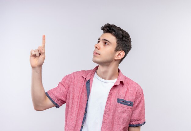 Mirando al lado caucásico joven vestido con camisa rosa apunta hacia arriba en la pared blanca aislada