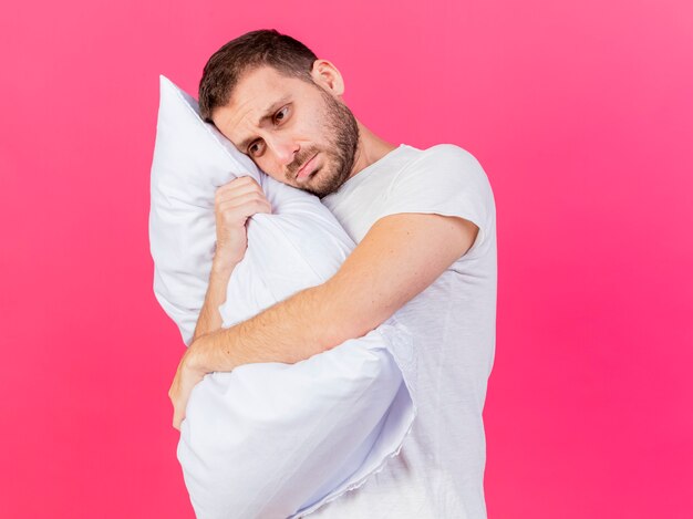 Mirando al lado complacido joven enfermo abrazó la almohada aislada sobre fondo rosa