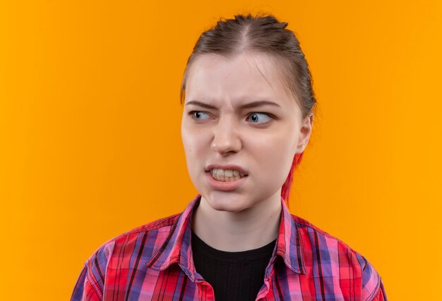 Mirando al lado confundido joven hermosa mujer con camisa roja en la pared amarilla aislada