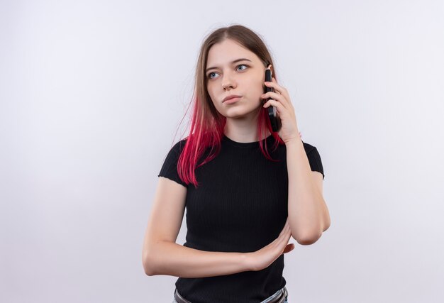 Mirando al lado hermosa joven vestida con camiseta negra habla por teléfono sobre fondo blanco aislado