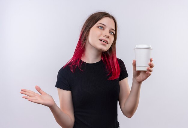 Mirando al lado hermosa joven vestida con camiseta negra sosteniendo una taza de café sobre fondo blanco aislado