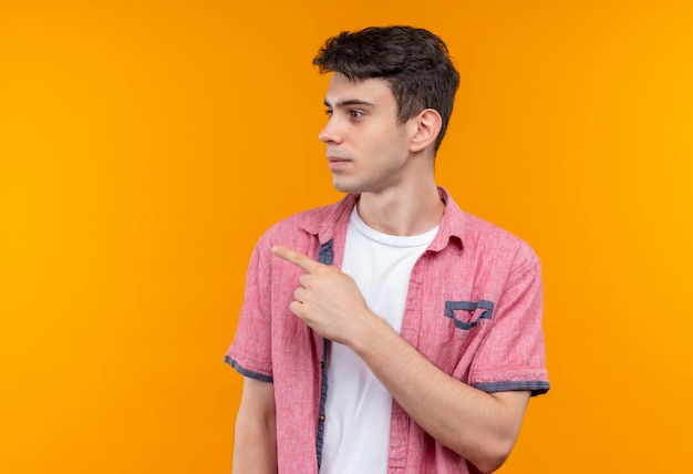 Foto gratuita mirando al lado del hombre joven caucásico con camisa rosa apunta al lado de la pared naranja aislada