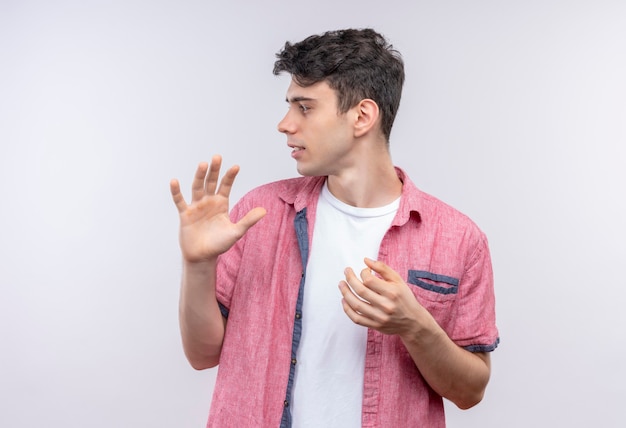 Mirando al lado del hombre joven caucásico con camisa rosa que muestra un gesto diferente en la pared blanca aislada