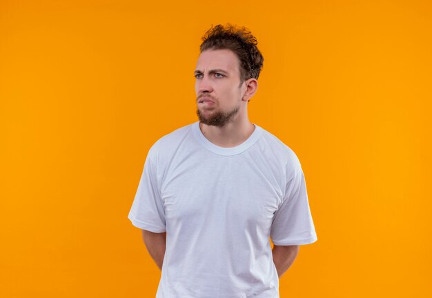 Mirando al lado joven con camiseta blanca mordiendo los labios sobre fondo naranja aislado