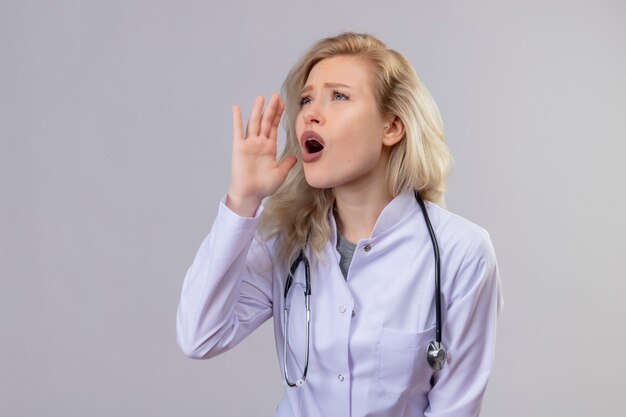 Mirando al lado joven médico con estetoscopio en bata médica susurra en la pared blanca