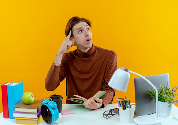 Mirando al lado pensando joven estudiante chico sentado en el escritorio