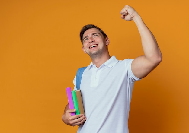 Foto gratuita mirando hacia arriba alegre joven apuesto estudiante vistiendo bolsa trasera levantando el puño aislado en la pared naranja