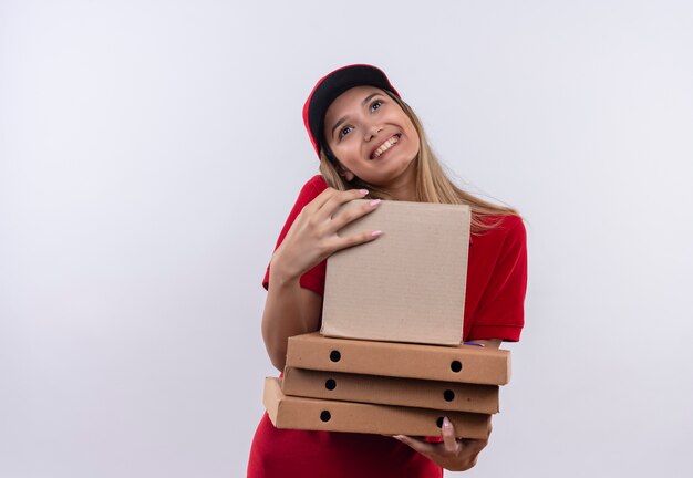 Foto gratuita mirando hacia arriba alegre joven repartidora vestida con uniforme rojo y gorra sosteniendo cajas aisladas sobre fondo blanco con espacio de copia