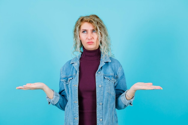 Mirando hacia arriba, la mujer rubia está abriendo sus manos sobre fondo azul.