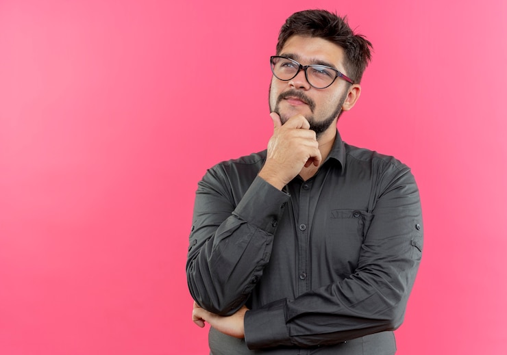 Foto gratuito mirando hacia arriba pensando joven empresario con gafas poniendo la mano en el mentón aislado en la pared rosa