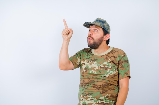 Foto gratuita mirando hacia arriba, el soldado está apuntando hacia arriba con el dedo índice sobre fondo blanco.