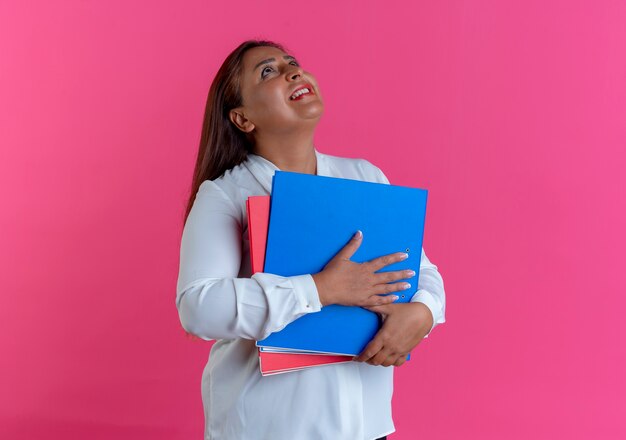 Mirando hacia arriba sonriente casual mujer de mediana edad caucásica sosteniendo la carpeta