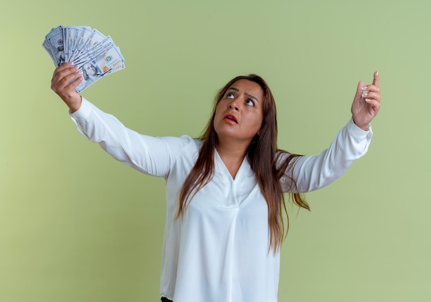 Foto gratuita mirando hacia arriba sorprendida mujer de mediana edad caucásica casual sosteniendo dinero en efectivo y apunta hacia arriba