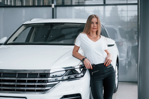 Mirando a la cámara. Chica y coche moderno en el salón. Durante el día en interiores. Comprar vehículo nuevo