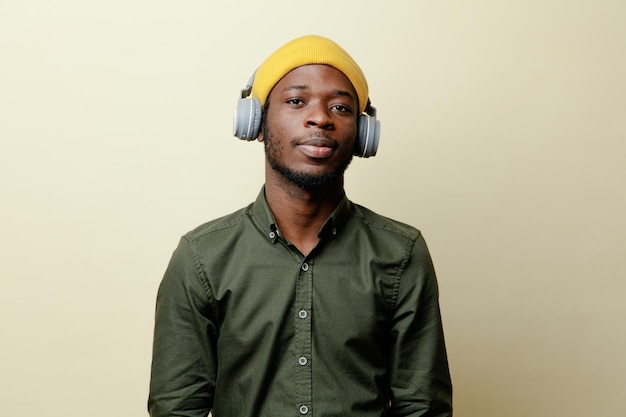 Mirando a la cámara, joven afroamericano con sombrero y auriculares con camisa verde aislada en fondo blanco