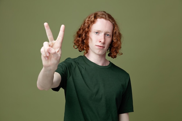 Mirando a la cámara que muestra el número de un joven apuesto que usa una camiseta verde aislado en un fondo verde