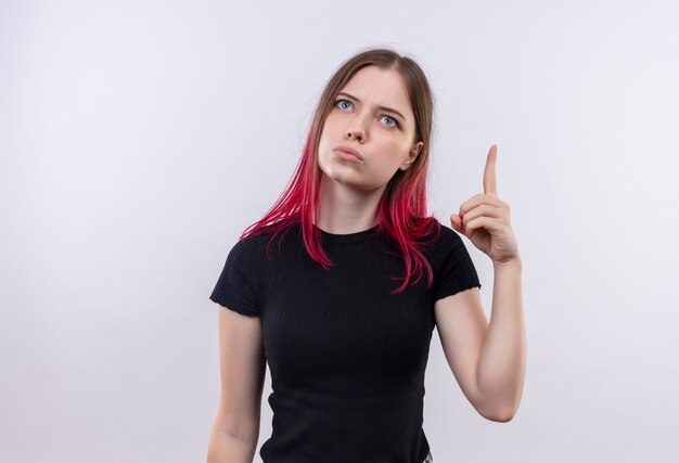 Mirando a la hermosa joven vestida con camiseta negra apunta con el dedo hacia arriba sobre fondo blanco aislado