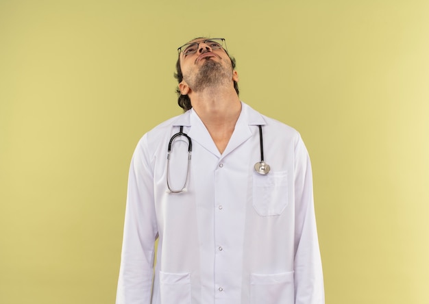 Foto gratuita mirando a un joven médico con gafas ópticas vistiendo una túnica blanca con estetoscopio