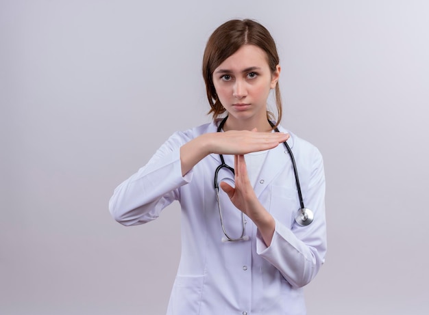 Mirando seriamente a la joven doctora vistiendo una bata médica y un estetoscopio y haciendo un gesto de tiempo de espera con espacio de copia