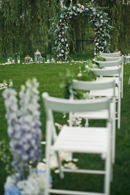 Mire de detrás en las sillas blancas que se colocan en el césped verde antes del altar de la boda