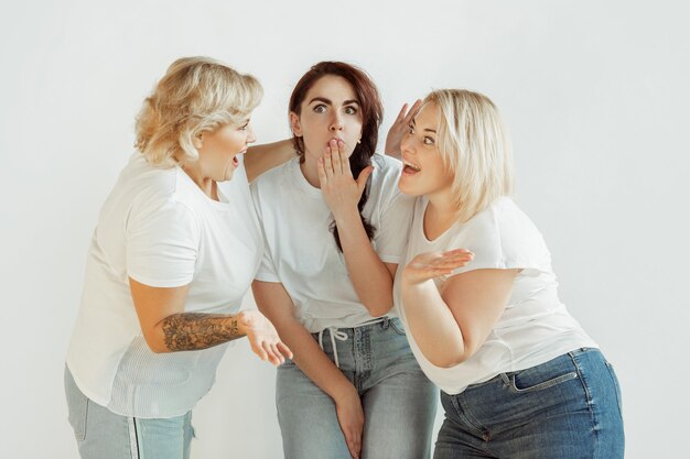 Misterios. Jóvenes mujeres caucásicas en ropa casual divirtiéndose juntos. Amigos posando sobre fondo blanco y riendo, se ve feliz, bien cuidado. Bodypositive, feminismo, amarse a sí mismo, concepto de belleza.