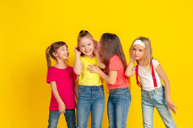 Misterios. Niños felices jugando y divirtiéndose juntos sobre fondo amarillo de estudio. Los niños caucásicos con ropa brillante se ven juguetones, riendo, sonriendo. Concepto de educación, infancia, emociones.