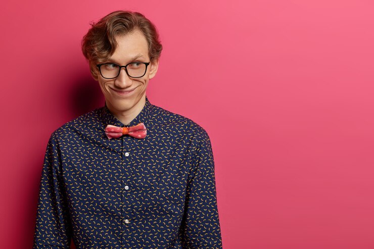 Foto gratuito misterioso hombre adulto feliz tiene una amplia sonrisa en la cara, concentrado a un lado, se encuentra en el interior sobre una pared rosada, tiene una agradable conversación con sus compañeros de trabajo, vestido formalmente, aislado sobre una pared rosa, espacio en blanco