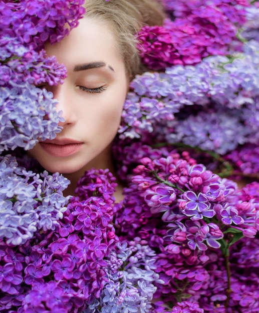 La mitad de la cara de la joven rubia caucásica con los ojos cerrados rodeada de un montón de lilas moradas y violetas, papel tapiz, melodía de primavera