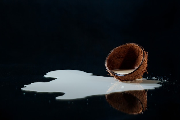 Foto gratuita la mitad de coco con leche sobre fondo negro.