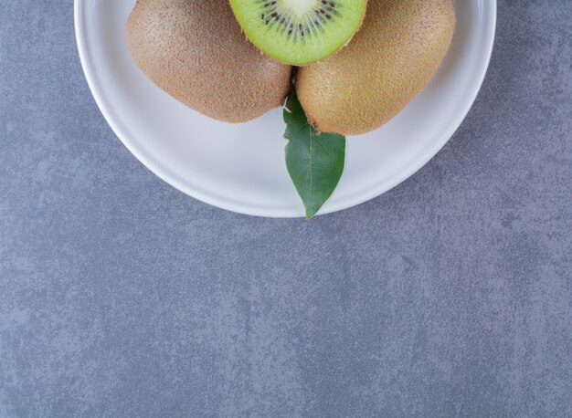 La mitad y los kiwis enteros en un plato sobre una mesa de mármol.