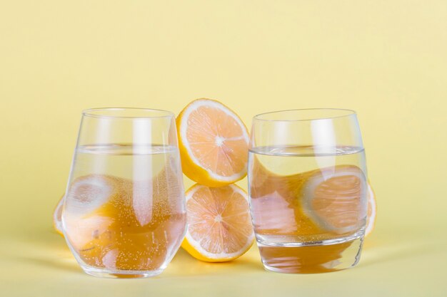 La mitad de limones y vasos de agua sobre fondo amarillo