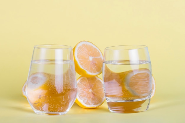 La mitad de limones y vasos de agua sobre fondo amarillo