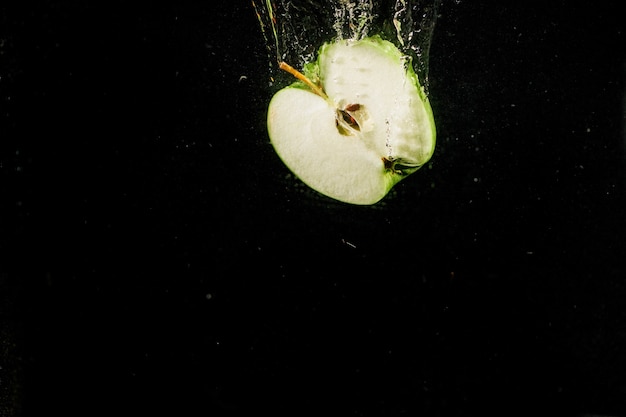 La mitad de la manzana cae en el agua sobre fondo negro