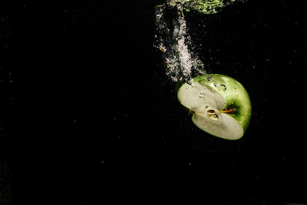 La mitad de la manzana verde salpica el agua mientras que cae