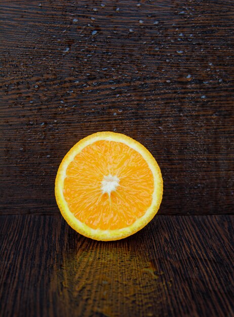 La mitad de naranja fresca sobre una superficie de madera oscura y húmeda