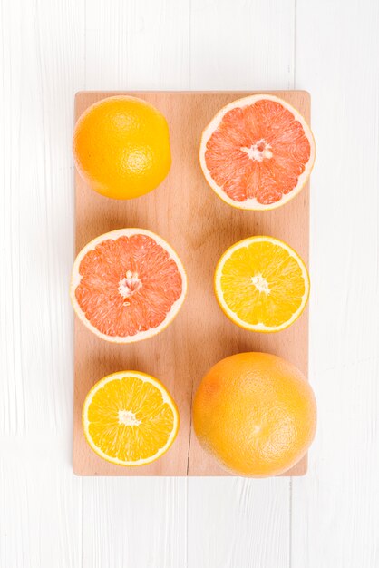 Una mitad de naranjas y pomelos en tabla de cortar sobre mesa blanca