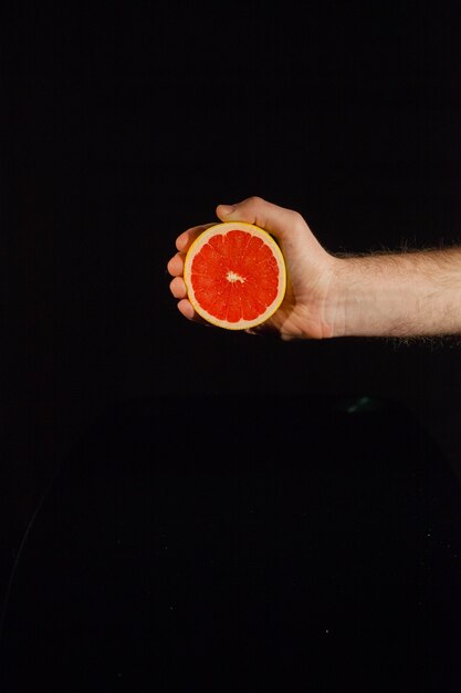 La mitad de un pomelo jugoso en la mano del hombre sobre fondo negro