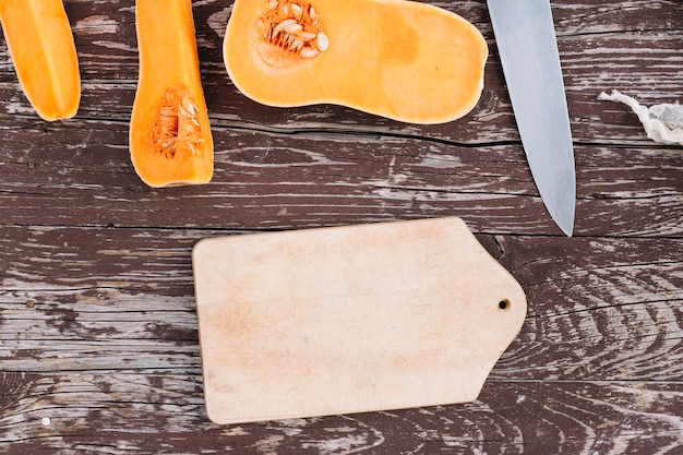 Mitades de calabaza cruda orgánica con tabla de cortar y cuchillo afilado en la parte superior de la mesa desgastada