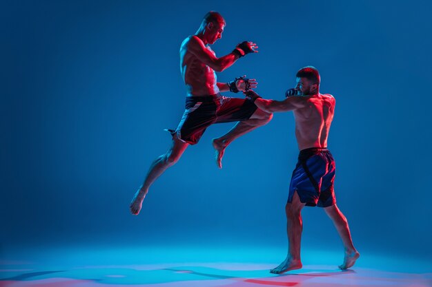 MMA. Dos luchadores profesionales de perforación o boxeo aislado en la pared azul en neón