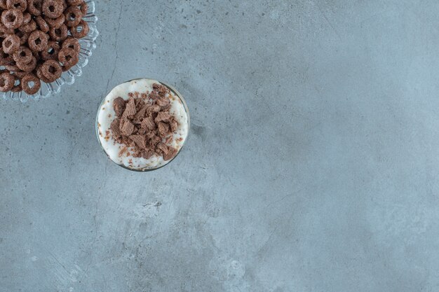 Moca de chocolate en un vaso junto al aro de maíz sobre un pedestal de vidrio, sobre el fondo azul.