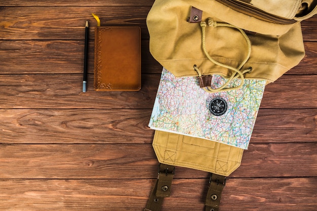 Mochila, mapa y brújula sobre fondo de madera con diario y pluma